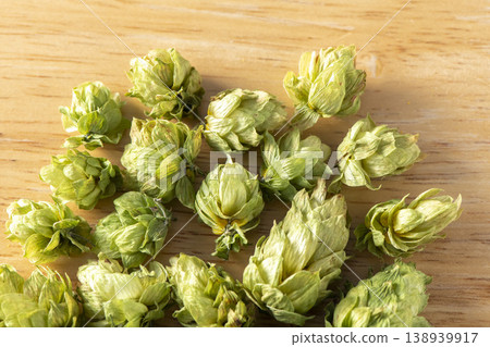 Dried hop cones are placed on a wooden table, conveying the aroma and bitterness of hops used as an ingredient in beer brewing. 138939917