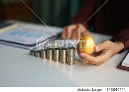 Rising stack of coins and golden eggs on the table. Businessman calculating dividend yield on the background for wealth management and investment concept. 138940521