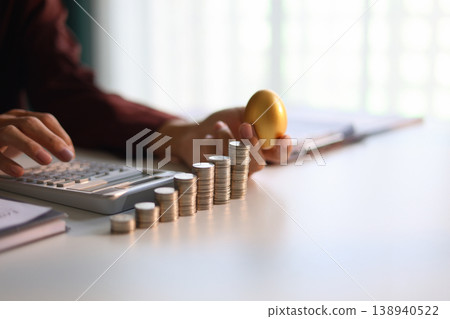 Rising stack of coins and golden eggs on the table. Businessman calculating dividend yield on the background for wealth management and investment concept. 138940522