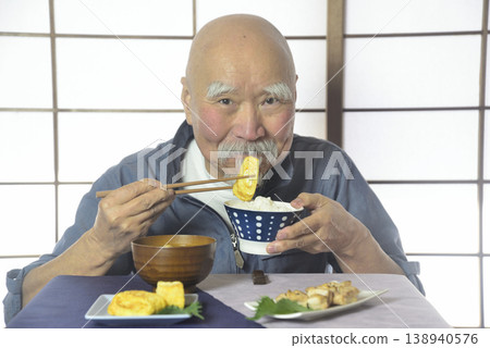 一位留著鬍子的老人面帶微笑地吃著飯。 138940576