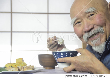 一位留著鬍子的老人面帶微笑地吃著飯。 一位留著鬍子的老人面帶微笑地吃著飯。 138940578