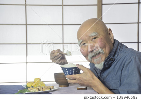 一位留著鬍子的老人面帶微笑地吃著飯。 138940582