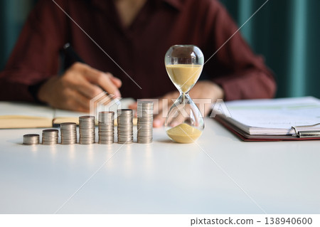 Rising stack of coins and running sand clock on the table. Growing of income, saving or return investment through time. Time and money concept. 138940600