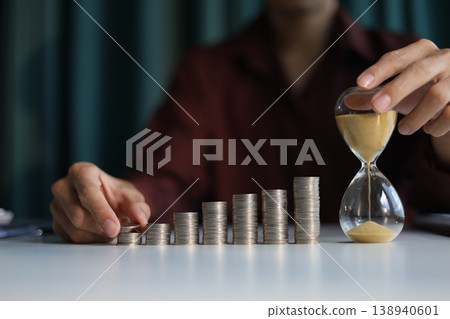 Rising stack of coins and running sand clock on the table. Growing of income, saving or return investment through time. Time and money concept. 138940601