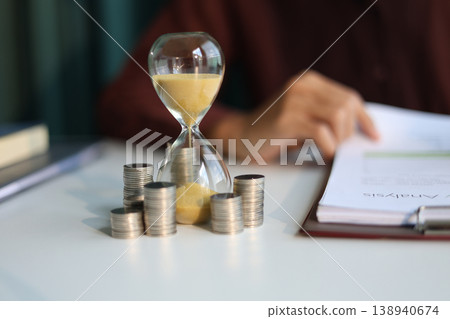 Coin stacks and sand clock on the table. Growing of income, saving or return investment through time. Time and money concept. 138940674