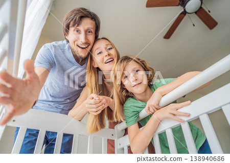 Parents and older brother looking into baby crib from infant point of view. Family smiling down at newborn with love and care. Sibling bonding, parenthood, childhood memory and connection concept Parents and older brother looking into baby crib from infant point of view. Family smiling down at newborn with love and care. Sibling bonding, parenthood, childhood memory and connection concept 138940686