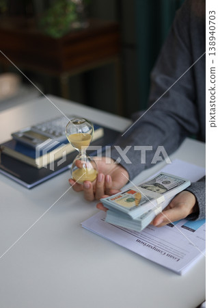 Time and money concept. Businessman holding cash and sand clock imply growth of income, saving or return investment through time. Time and money concept. Businessman holding cash and sand clock imply growth of income, saving or return investment through time. 138940703