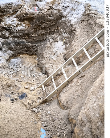 A deep trench in the ground with an extension ladder at a construction site A deep trench in the ground with an extension ladder at a construction site 138940937