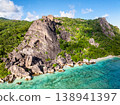 Imposing rocky cliffs rise above lush greenery, with turquoise waters at the base. Seychelles, La Digue. 138941397