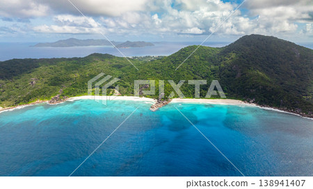 Turquoise waters meeting tropical green hills on a sunny coastline. La Digue, Seychelles. Turquoise waters meeting tropical green hills on a sunny coastline. La Digue, Seychelles. 138941407