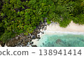 Lush green forest bordering a sandy beach with scattered rocks, leading into the turquoise water. Butzel Beach. Seychelles, Mahe. 138941414