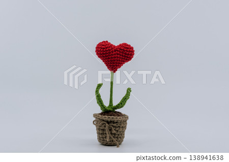 A small crocheted flowerpot with a red heart-shaped flower placed on a white background. A small crocheted flowerpot with a red heart-shaped flower placed on a white background. 138941638