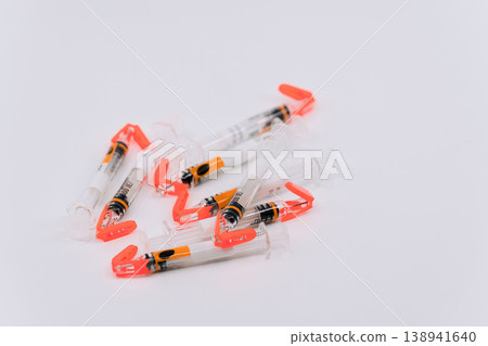 Disposable syringes with orange safety caps scattered on a white background. 138941640