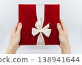 A person holding a red gift box in both hands in front of a white background. 138941644