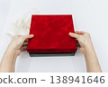 The image shows someone lifting and opening the lid of a red gift box with both hands. 138941646