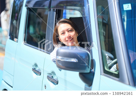 A Japanese woman smiles as she looks out the window from the driver's seat of a car. A Japanese woman smiles as she looks out the window from the driver's seat of a car. 138942161