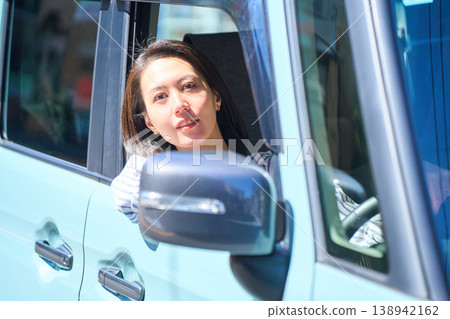 A Japanese woman smiles as she looks out the window from the driver's seat of a car. A Japanese woman smiles as she looks out the window from the driver's seat of a car. 138942162