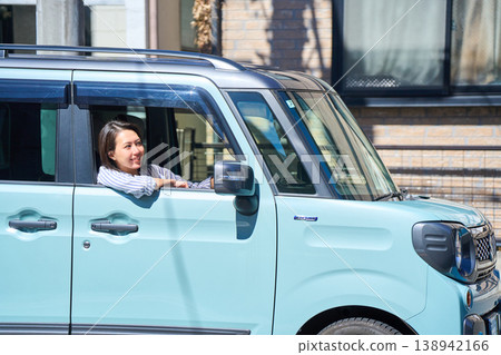 A Japanese woman smiles as she looks out the window from the driver's seat of a car. A Japanese woman smiles as she looks out the window from the driver's seat of a car. 138942166