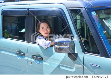 A Japanese woman smiles as she looks out the window from the driver's seat of a car. A Japanese woman smiles as she looks out the window from the driver's seat of a car. 138942171