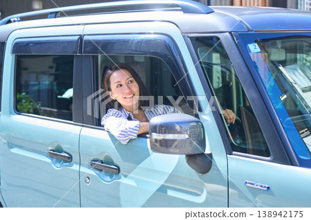 一位日本女子坐在汽車駕駛座上，望著窗外，帶著微笑。 138942175
