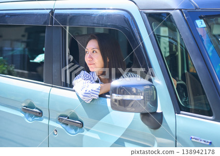 A Japanese woman smiles as she looks out the window from the driver's seat of a car. 138942178
