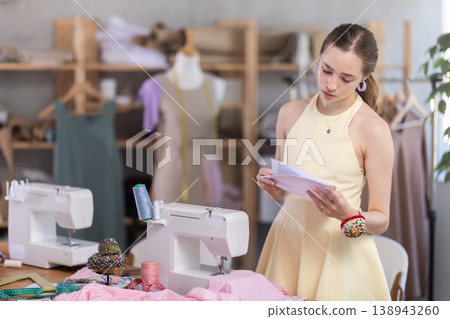 Upset young woman seamstress with documents in workshop Upset young woman seamstress with documents in workshop 138943260