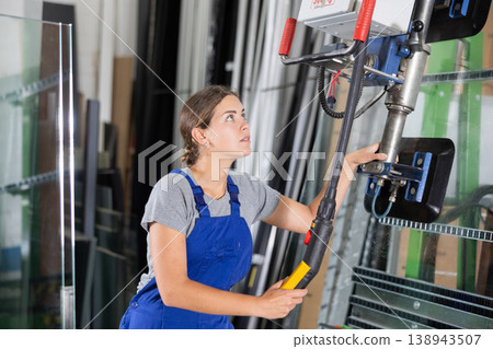 Female worker moves window panes using lifting mechanism in an industrial workshop Female worker moves window panes using lifting mechanism in an industrial workshop 138943507