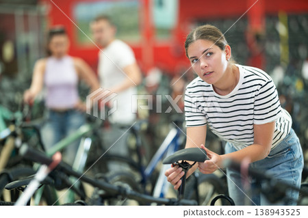 Young woman in bicycle shop choosing new sport bike and selecting model seat 138943525