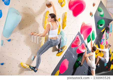 Young woman climbs steep artificial wall in sports complex and trains endurance 138943526