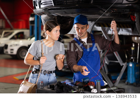 Guy mechanic checking woman client's car with measuring device Guy mechanic checking woman client's car with measuring device 138943533