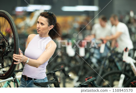 Young woman selects bicycle in sporting goods store, checking wheel quality using smartphone 138943570