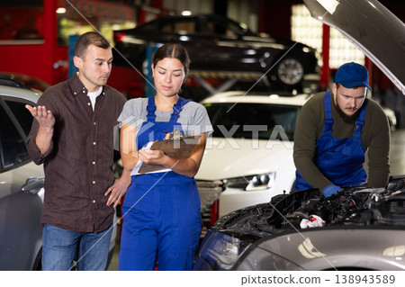 Female worker of auto service speaking to male client concerning her notes on paper Female worker of auto service speaking to male client concerning her notes on paper 138943589