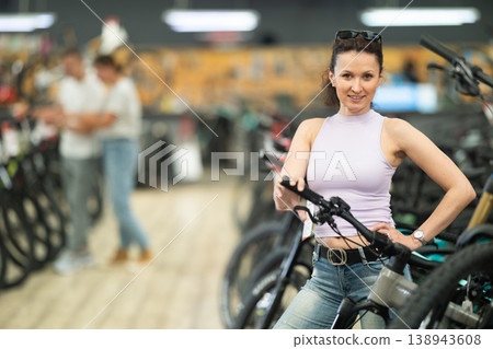 Smiling woman examining handlebar of new bicycle in shop Smiling woman examining handlebar of new bicycle in shop 138943608