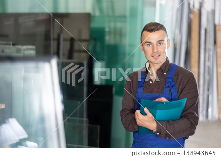 Experienced worker checks the quality of made window glass in an industrial workshop, marks the data in documents Experienced worker checks the quality of made window glass in an industrial workshop, marks the data in documents 138943645