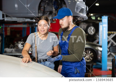 Happy young girl touching surface of her car standing next to male car mechanic Happy young girl touching surface of her car standing next to male car mechanic 138943685
