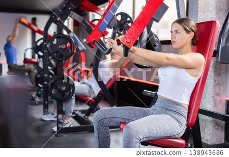 Young woman trains her arm muscles on machine Young woman trains her arm muscles on machine 138943686