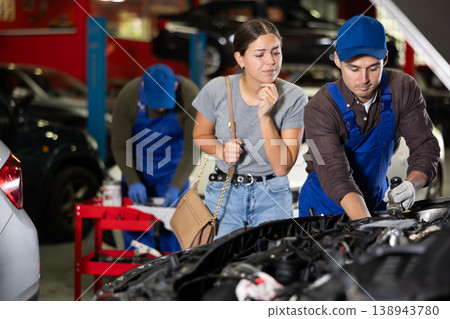 Skilled male auto mechanic controlling automobile detail while young girl looking at it disappointedly Skilled male auto mechanic controlling automobile detail while young girl looking at it disappointedly 138943780