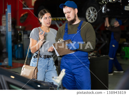Male worker of auto service speaking to female client concerning his notes on paper 138943819