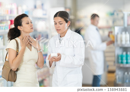 Young female pharmacist offering medicine to woman suffering from pain 138943881
