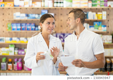 Female pharmacist consulting young guy about medicament according to recipe Female pharmacist consulting young guy about medicament according to recipe 138943947