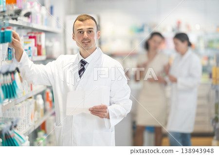 Positive male pharmacist in medical uniform posing while working in pharmacy 138943948