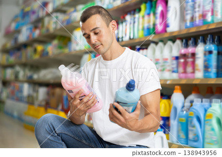 Man customer in store chooses package of laundry detergent Man customer in store chooses package of laundry detergent 138943956