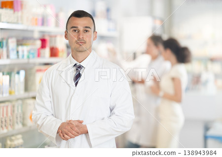Positive male pharmacist in medical uniform posing while working in pharmacy Positive male pharmacist in medical uniform posing while working in pharmacy 138943984