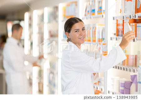 In chemist shop, woman consultant designs showcase with beauty care cosmetics 138943985
