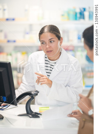 Female pharmacist at the cash register selling medicine to pharmacy visitor 138943991