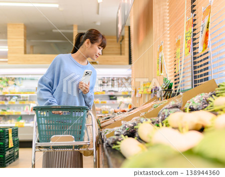 A woman chooses vegetables at the supermarket. 138944360