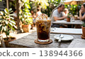Iced coffee enjoyed on a summer cafe terrace, with cream topping and a metal straw. 138944366