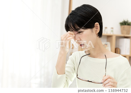 一位日本女性休息時，因眼睛疲勞而按壓眼角，並摘下了眼鏡。 138944732