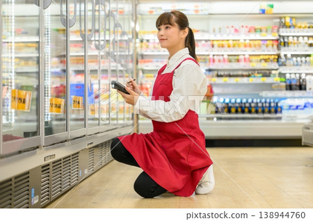 A female store clerk checking the refrigerated display case. A female store clerk checking the refrigerated display case. 138944760