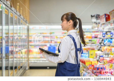 A female store clerk at the supermarket holding a tablet 138944943